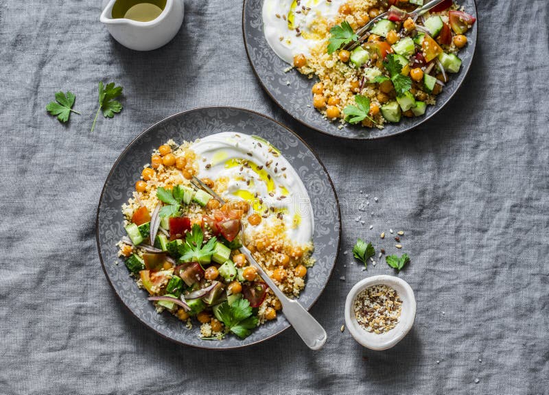 Garbanzos y cuscús condimentados con la ensalada y el yogur griego en un fondo gris, visión superior del ` s del pastor imagenes de archivo Garbanzos y cuscús condimentados con la ensalada y el yogur griego en un fondo gris, visión superior del ` s del pastor imagenes de archivo