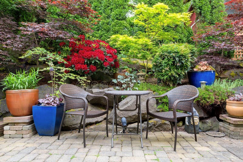 Garden Backyard Landscaping with Bistro Furniture springtime. Garden backyard with lush plants landscaping and stone paver patio hardscape with wicker bistro royalty free stock image