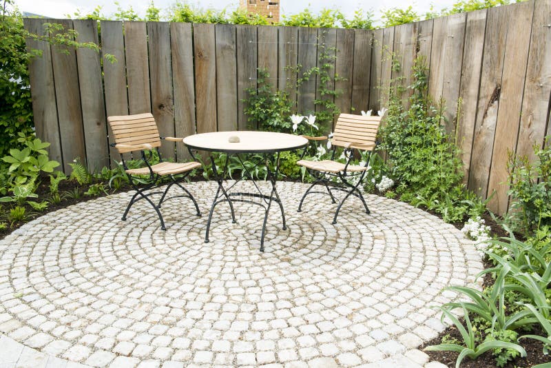 Garden patio with two chairs and round table in front of flowerbed and wooden planks