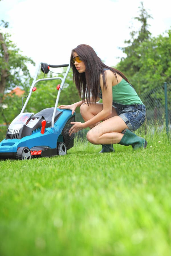 Garden work, woman mowing grass with lawnmower. 