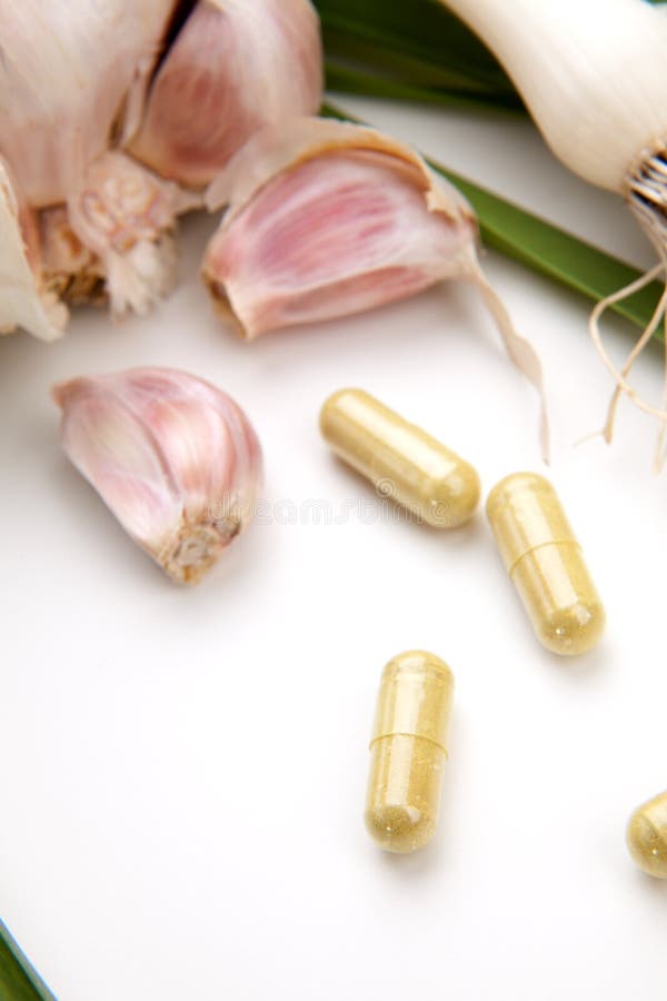 Closeup of garlic extract pills and fresh garlic leaves and cloves best suited for health, anti-cholesterol and alternative medicine ads. Green herbal drug medicine stock images, royalty-free photos and pictures