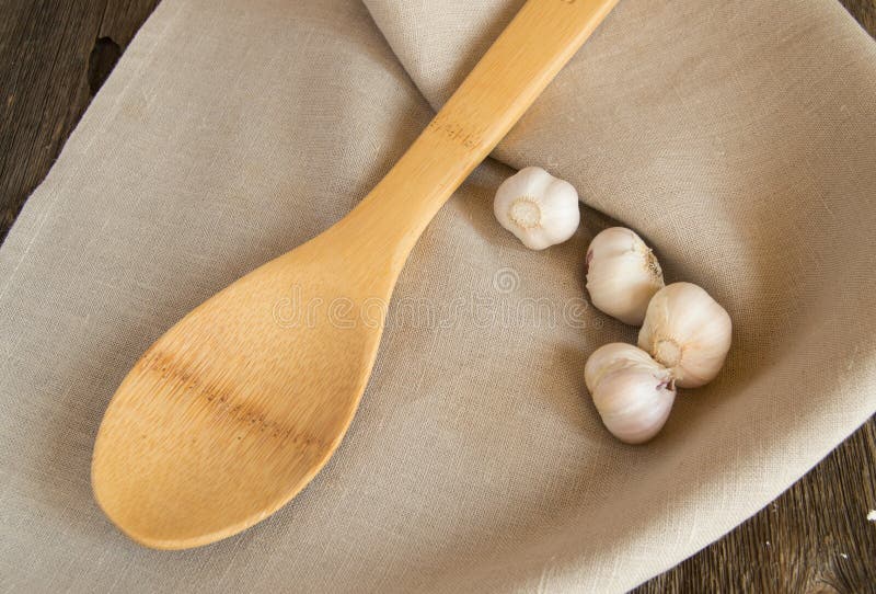 Garlic and a wooden spoon lying on a linen napkin. Old dark farm table, copy space.