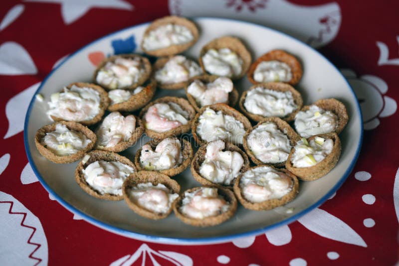 Cocktail bites aka finger foods made with Finnish dried rye bread filled with scrimp filling. Healthy and delicious party snack photographed on a table with Christmas themed red and white table cloth. Color closeup. Cocktail bites aka finger foods made with Finnish dried rye bread filled with scrimp filling. Healthy and delicious party snack photographed on a table with Christmas themed red and white table cloth. Color closeup.