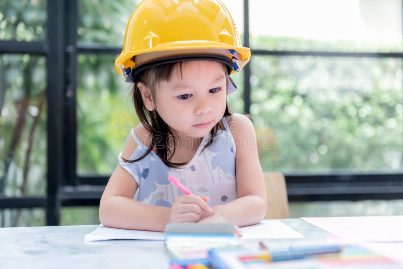 Garota asiática de 4 anos usando capacete de engenheiro está colorindo com intenção imagem de stock