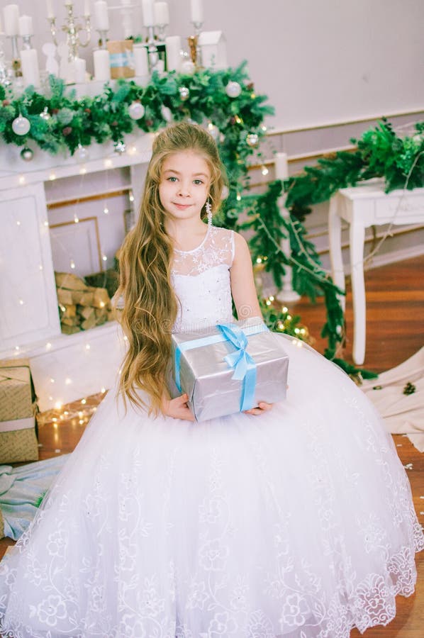 Garota bonita de cabelo comprido com um vestido branco de bola perto da árvore de Natal em vestidos de férias com presentes e con foto de stock royalty free Garota bonita de cabelo comprido com um vestido branco de bola perto da árvore de Natal em vestidos de férias com presentes e con foto de stock royalty free