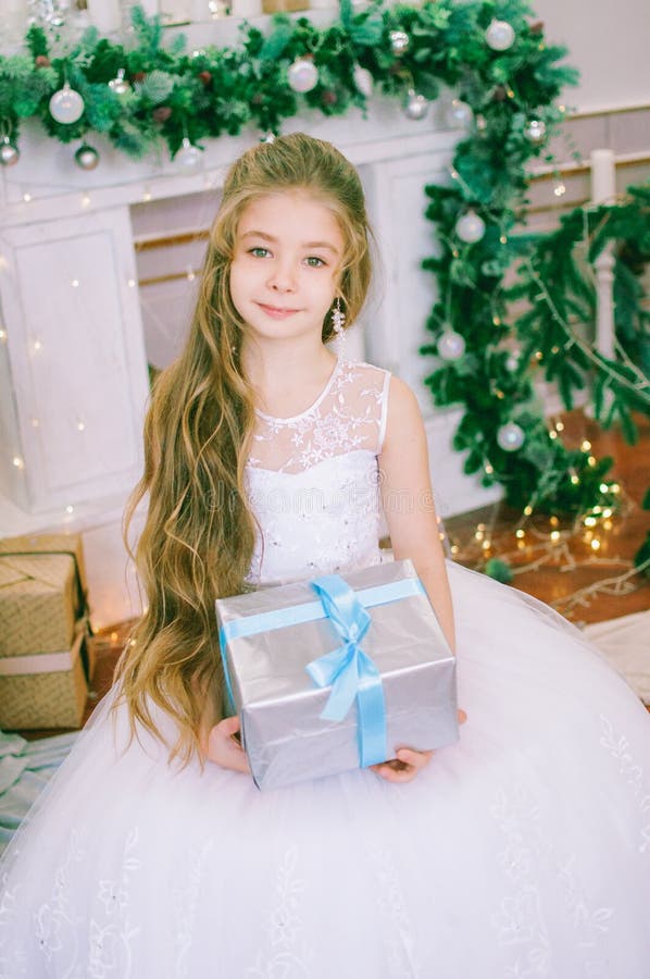 Garota bonita de cabelo comprido com um vestido branco de bola perto da árvore de Natal em vestidos de férias com presentes e con imagem de stock Garota bonita de cabelo comprido com um vestido branco de bola perto da árvore de Natal em vestidos de férias com presentes e con imagem de stock