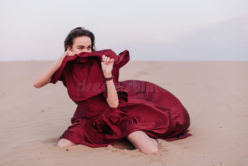 Young, slender, beautiful girl with red cloth sits in the wind in the desert. Young, slender, beautiful girl with red cloth sits in the wind in the desert