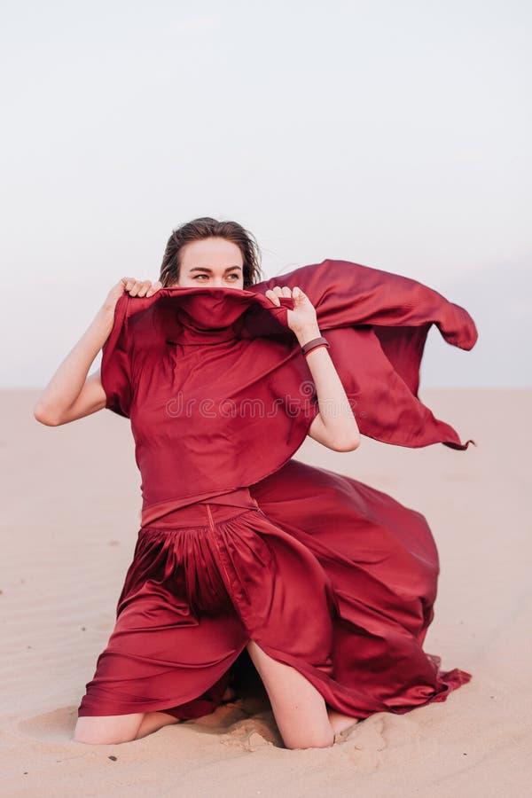 Young, slender, beautiful girl with red cloth sits in the wind in the desert. Young, slender, beautiful girl with red cloth sits in the wind in the desert