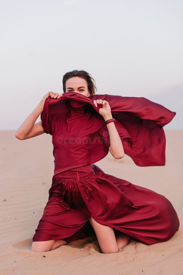 Young, slender, beautiful girl with red cloth sits in the wind in the desert. Young, slender, beautiful girl with red cloth sits in the wind in the desert