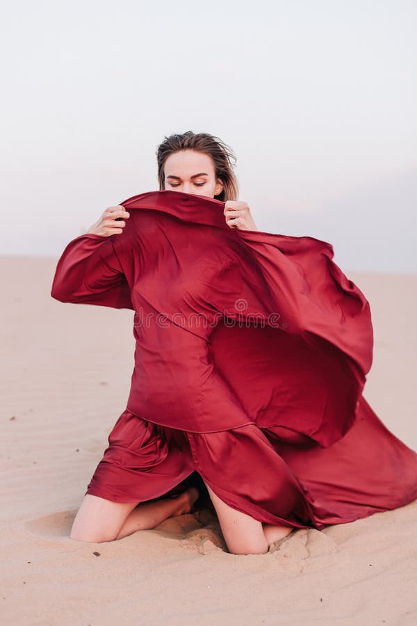 Young, slender, beautiful girl with red cloth sits in the wind in the desert. Young, slender, beautiful girl with red cloth sits in the wind in the desert