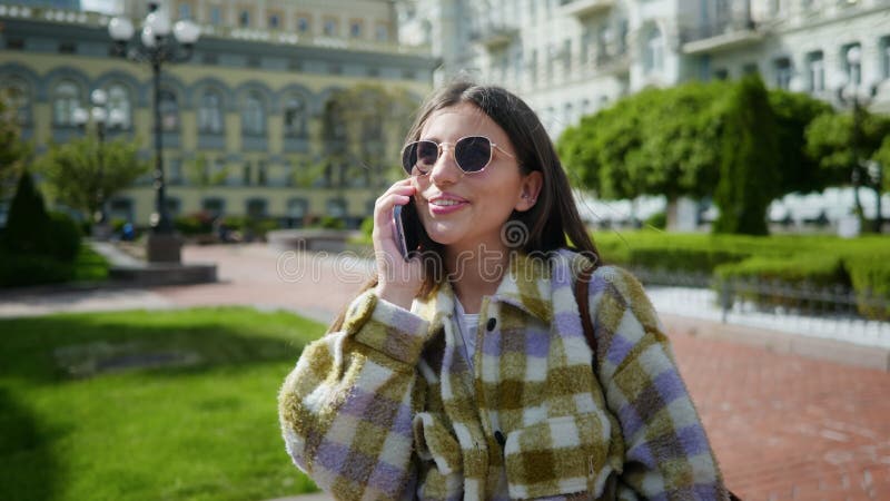 A garota está no telefone. uma garota sorrindo atendendo seu celular. menina falando no smartphone lá fora