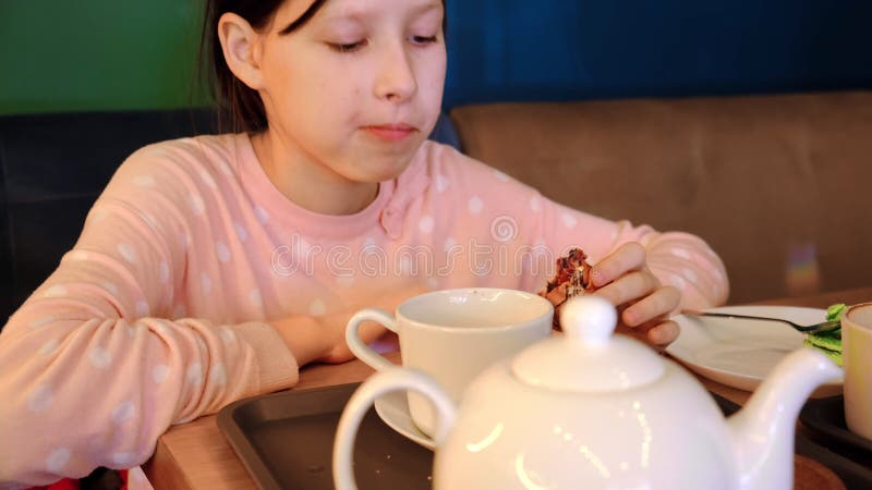 Garota feliz sorrindo bebe chá com macarrão de bolo no café. adolescente sentada à mesa e comendo no café