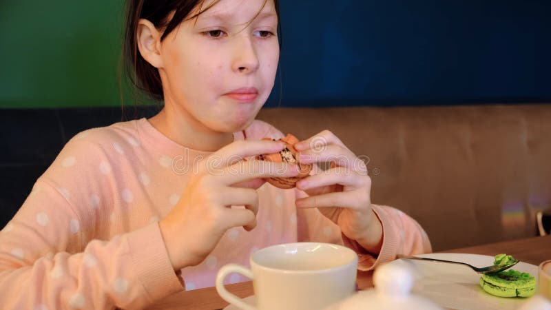 Garota feliz sorrindo bebe chá com macarrão de bolo no café. adolescente sentada à mesa e comendo no café