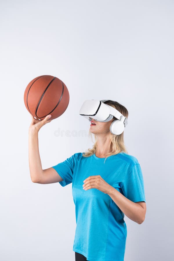 Girl wearing visual reality glasses and casual cloth and holding basketball. Caucasian woman playing basketball while standing at pink background at sport arena hologram. Innovation. Contraption. Girl wearing visual reality glasses and casual cloth and holding basketball. Caucasian woman playing basketball while standing at pink background at sport arena hologram. Innovation. Contraption.