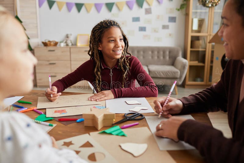 Portrait of smiling African-American girl looking at female teacher while enjoying art and craft class in school, copy space. Portrait of smiling African-American girl looking at female teacher while enjoying art and craft class in school, copy space
