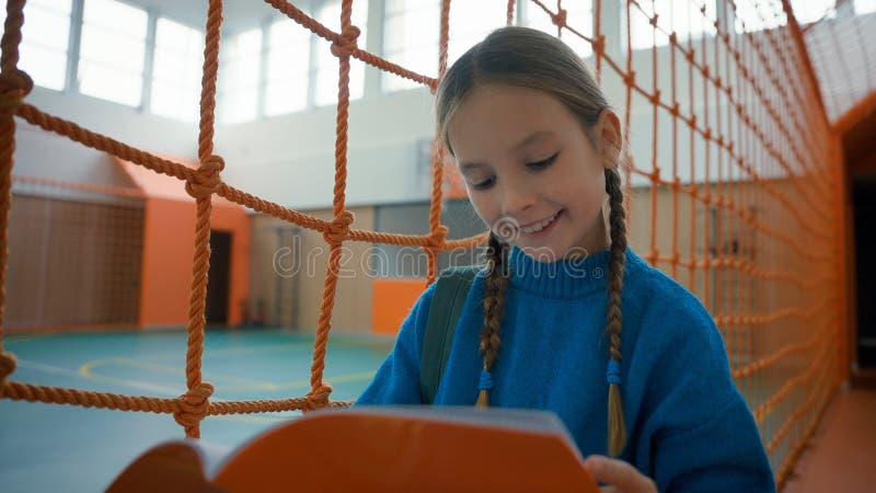 Little girl studying in gym school inside education self-study reading textbook preparing for lessons exam task test schoolgirl learner elementary age kid pupil female child copybook subject knowledge. High quality 4k footage. Little girl studying in gym school inside education self-study reading textbook preparing for lessons exam task test schoolgirl learner elementary age kid pupil female child copybook subject knowledge. High quality 4k footage