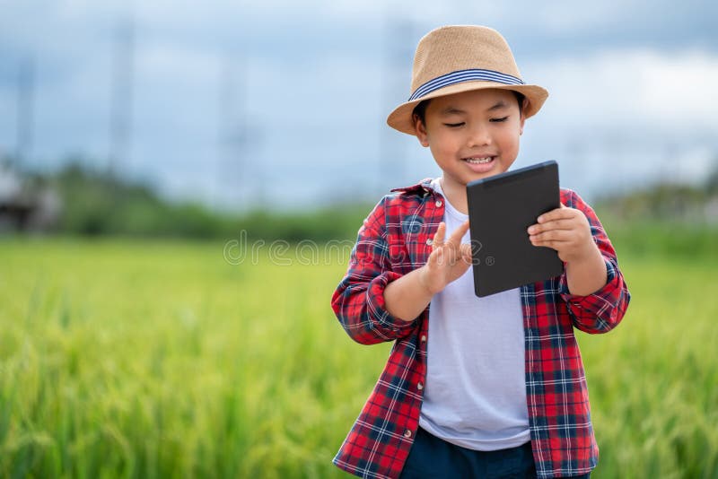 Garotinho asiático olhando tablet e interessado em aprender o ambiente do conceito de educação dos campos verdes fora do