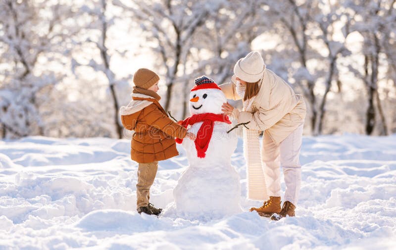 Garotinho bonitinho fazendo boneco de neve com a mãe no parque de inverno