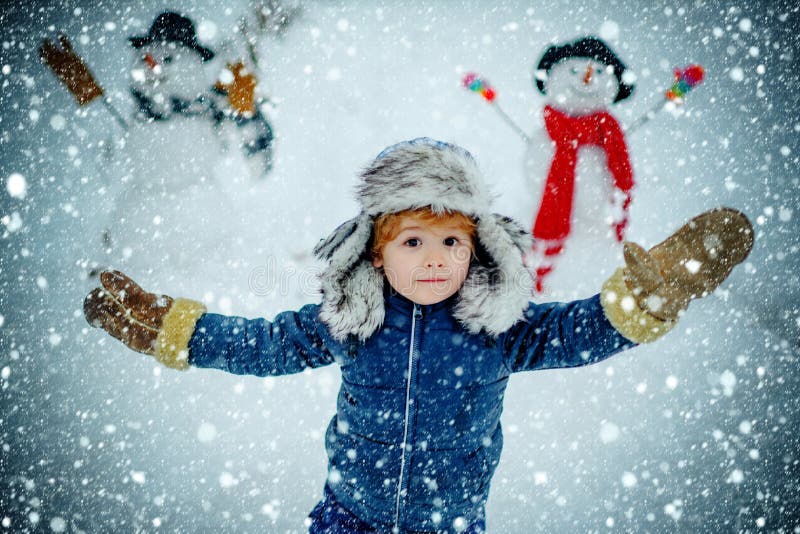 Garotinho brincando com boneco de neve no parque de inverno Retrato ao ar livre de um filho pequeno em um frio inverno ensolarado foto de stock royalty free Garotinho brincando com boneco de neve no parque de inverno Retrato ao ar livre de um filho pequeno em um frio inverno ensolarado foto de stock royalty free