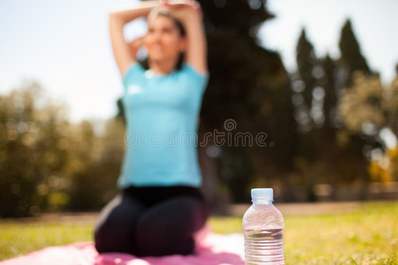 Garrafa de água com uma mulher a alongar-se ao fundo fotografia de stock royalty free