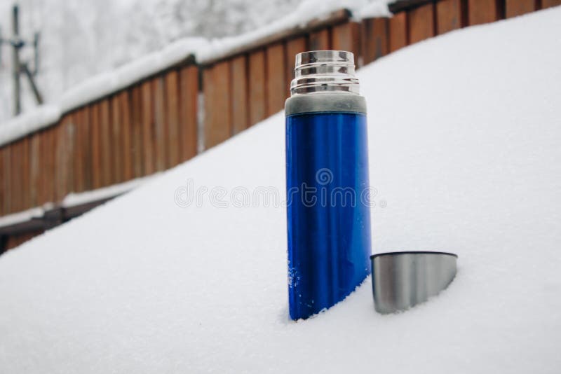 Garrafa térmica de prata azul do close-up com café ou chá na neve no pátio traseiro Feriados de inverno, conceito quente das bebi fotografia de stock Garrafa térmica de prata azul do close-up com café ou chá na neve no pátio traseiro Feriados de inverno, conceito quente das bebi fotografia de stock