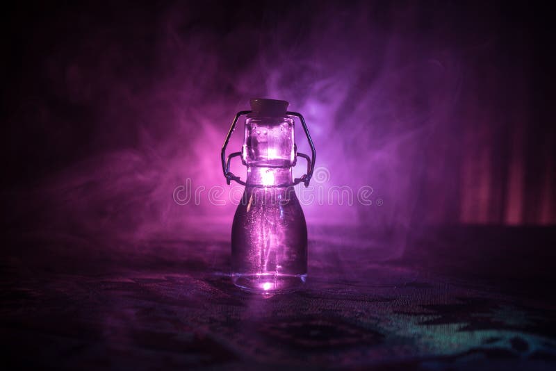 Antique and vintage glass bottle on dark foggy background with light. Poison or magic liquid concept. Antique and vintage glass bottle on dark foggy background with light. Poison or magic liquid concept.