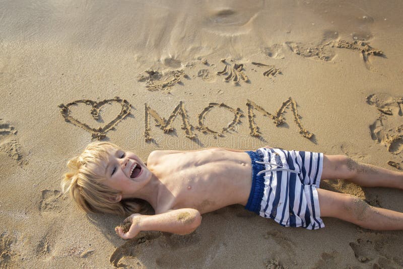 cheerful boy 5-6 years old son having fun on beach. heart is drawn on the sand and the word mom is written. Positive human emotions, feelings, joy, happy childhood. gift from a child for Mother's Day. cheerful boy 5-6 years old son having fun on beach. heart is drawn on the sand and the word mom is written. Positive human emotions, feelings, joy, happy childhood. gift from a child for Mother's Day