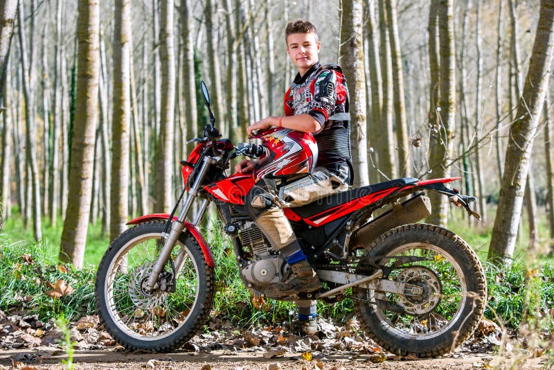 Garçon de l'adolescence beau s'asseyant sur la motocyclette de motocross photographie stock libre de droits Garçon de l'adolescence beau s'asseyant sur la motocyclette de motocross photographie stock libre de droits