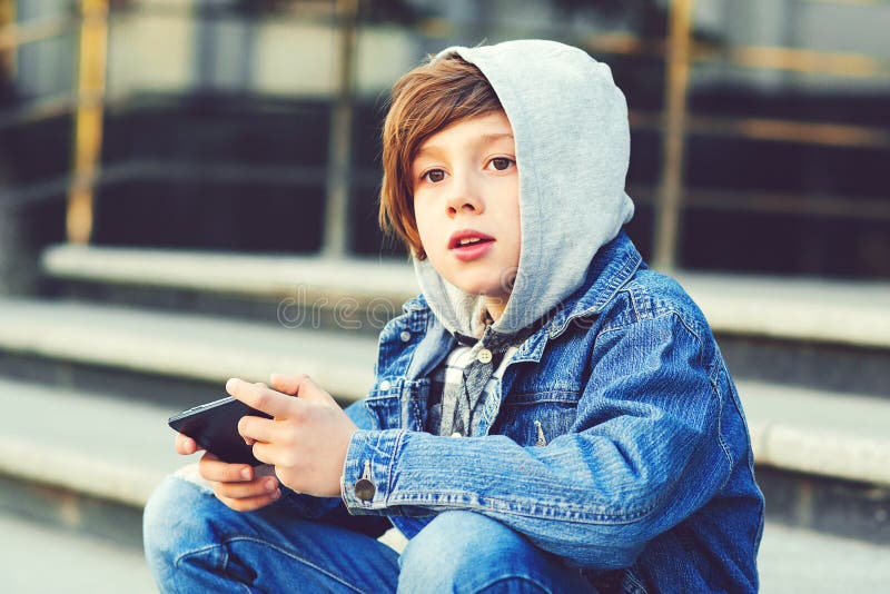 Garçon de la préadolescence à l'aide du smartphone à l'extérieur de l'école. Garçon malin jouant le jeu au téléphone. Écolier fais photographie stock