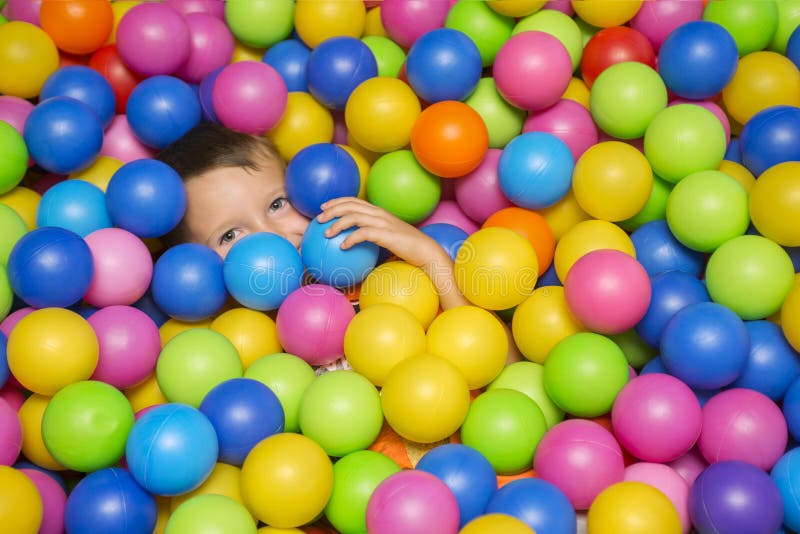 Garçon de sourire mignon dans la piscine de boule d'éponge regardant l'appareil-photo Enfant jouant avec les boules colorées dans image libre de droits Garçon de sourire mignon dans la piscine de boule d'éponge regardant l'appareil-photo Enfant jouant avec les boules colorées dans image libre de droits