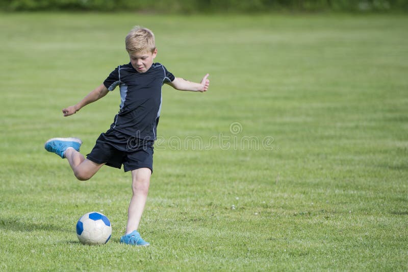 Garçon donnant un coup de pied la bille de football photographie stock Garçon donnant un coup de pied la bille de football photographie stock