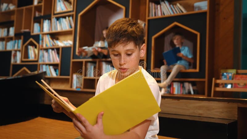 Garçon lisant un livre pendant que groupe d'étudiants intelligents assis à la bibliothèque. érudition. banque de vidéos