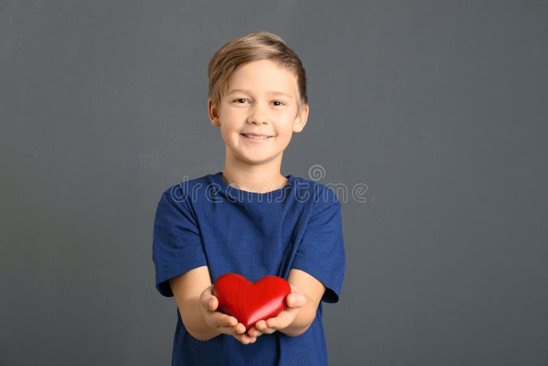 Garçon mignon tenant le coeur en bois sur le gris images stock Garçon mignon tenant le coeur en bois sur le gris images stock
