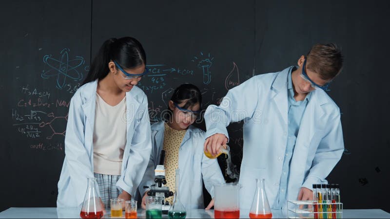 Garçon mélange liquide dans le bécher pendant que l'étudiant diversifié fait l'expérience. édification clips vidéos