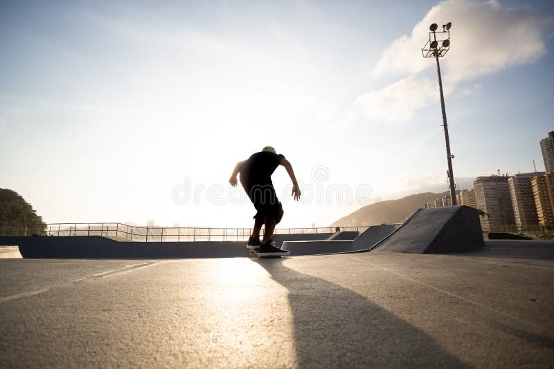 Garçon pratiquant le skateboard au coucher du soleil images stock