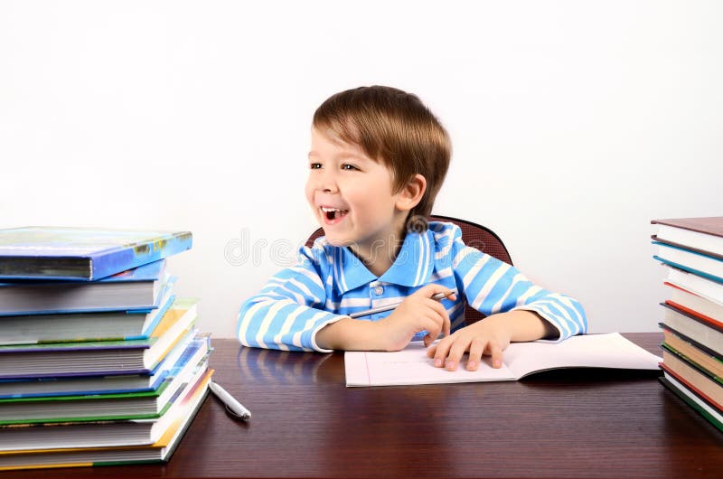 Garçon riant s'asseyant au bureau avec beaucoup de livres images stock Garçon riant s'asseyant au bureau avec beaucoup de livres images stock