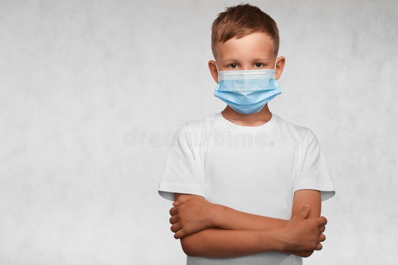 Serious boy with crossed arms weared in surgical mask and white t-shirt on a white background.   Covid-19, flu, or pollution. With place for your text. Serious boy with crossed arms weared in surgical mask and white t-shirt on a white background.   Covid-19, flu, or pollution. With place for your text.