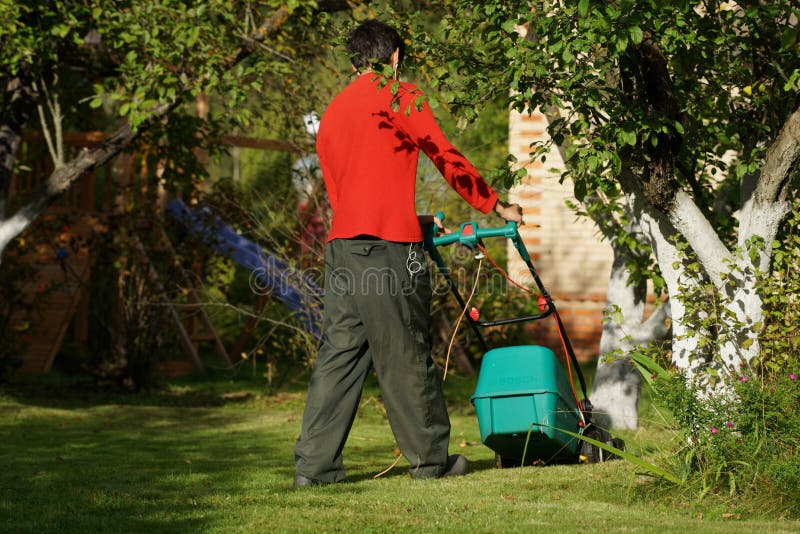 Garçon tondre la pelouse avec la tondeuse à gazon image stock