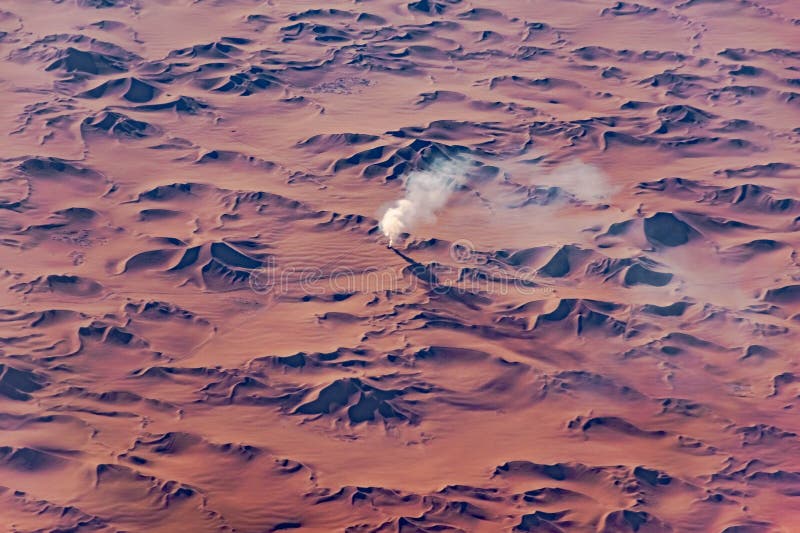 Bílý plyn kouř přichází ven z díra v střední z načervenalý písek duny v dálce v poušť z alžírsko.