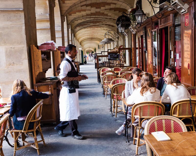 A Parisian restaurant in the Place des Vosges, Paris, France. A waiter is attending to customers seated at a table outside. A Parisian restaurant in the Place des Vosges, Paris, France. A waiter is attending to customers seated at a table outside.