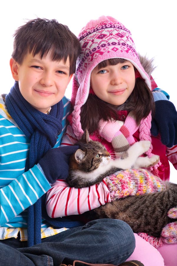 A studio view of a young boy and girl wearing winter hat, scarf and mittens, holding a brown cat. White background. A studio view of a young boy and girl wearing winter hat, scarf and mittens, holding a brown cat. White background.