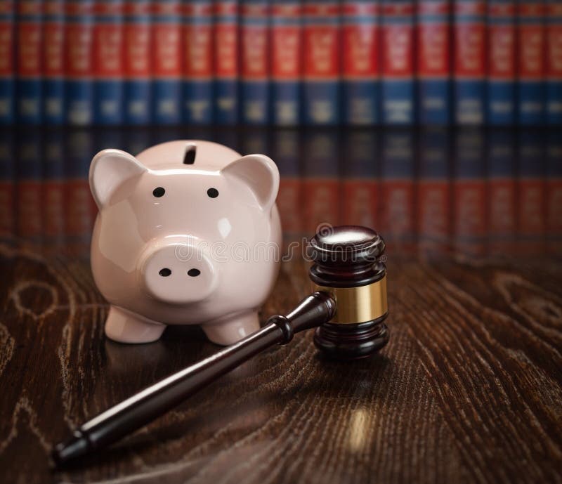 Gavel and Piggy Bank on Wooden Table With Law Books In Background. Gavel and Piggy Bank on Wooden Table With Law Books In Background.