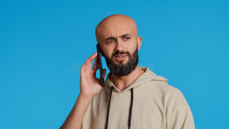 Middle eastern guy chatting with friends on phone call, answering smartphone while standing over blue background. Modern man discussing something on a remote network. Camera 2. Handheld shot. Middle eastern guy chatting with friends on phone call, answering smartphone while standing over blue background. Modern man discussing something on a remote network. Camera 2. Handheld shot.