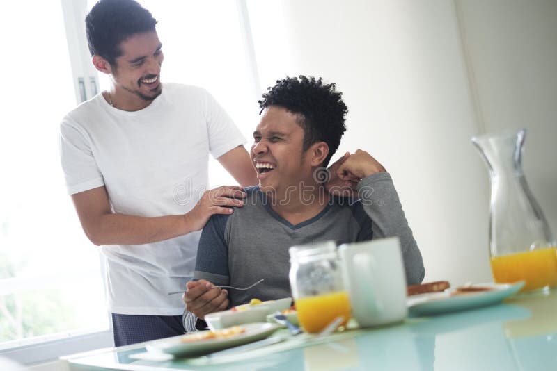 Homosexual couple, gay people, same sex marriage between hispanic men. Happy male partners eating breakfast at home in the morning and laughing. Homosexual couple, gay people, same sex marriage between hispanic men. Happy male partners eating breakfast at home in the morning and laughing