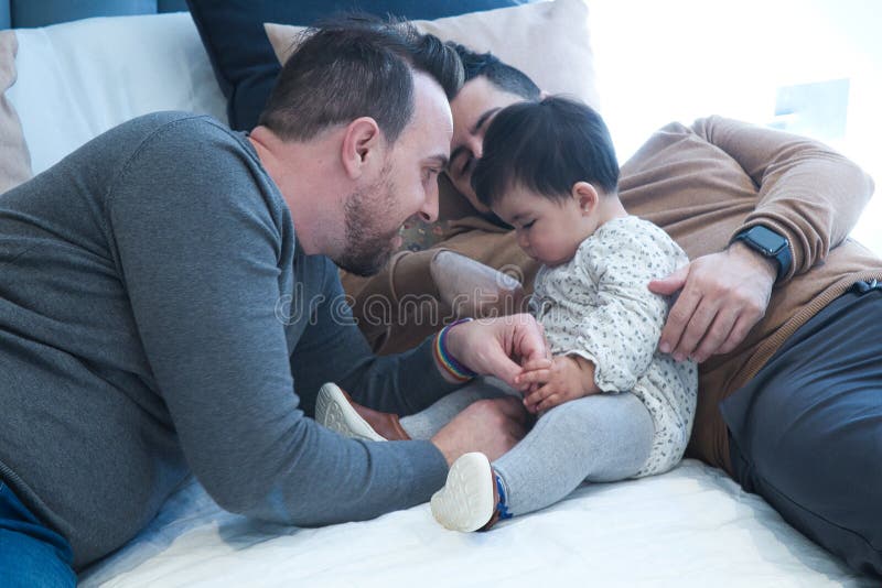 Gay Couple Playing with Their Daughter on the Marriage Bed in Their Home Stock Photo