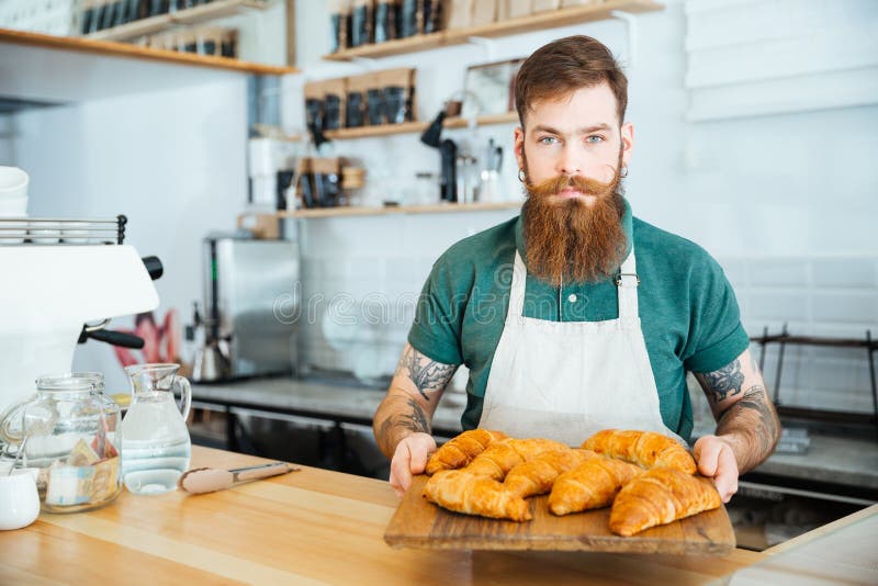 Gebaarde barista die en houten raad met croissants bevinden zich houden royalty-vrije stock fotografie Gebaarde barista die en houten raad met croissants bevinden zich houden royalty-vrije stock fotografie