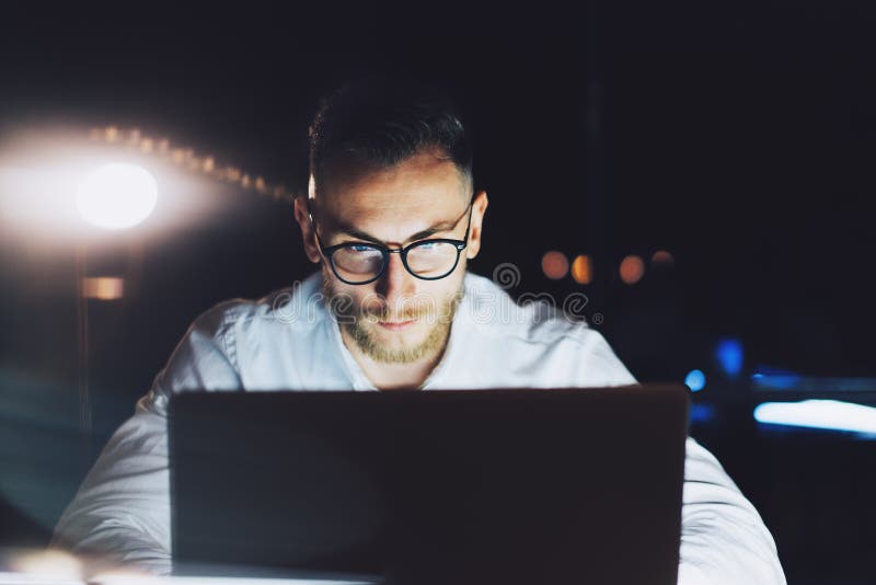 Gebaarde zakenman die glazen dragen die aan modern zolderbureau bij nacht werken Mens die het eigentijdse notitieboekje texting g stock afbeelding Gebaarde zakenman die glazen dragen die aan modern zolderbureau bij nacht werken Mens die het eigentijdse notitieboekje texting g stock afbeelding