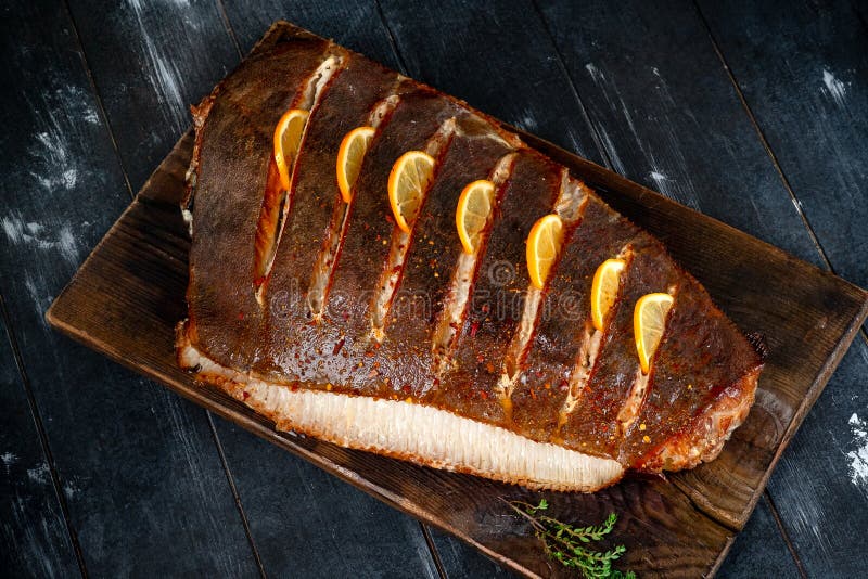 Gebackene Heilbuttfische mit Zitrone selbst auf einem hölzernen Brett auf einem dunklen Hintergrundmeeresfrüchteheißen geraucht stockbild