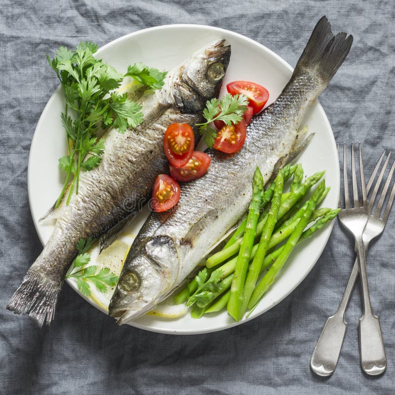 Gebackener Wolfsbarsch mit Spargel und Tomaten Lebensmittelkonzept der gesunden Diät auf einem grauen Hintergrund stockbild Gebackener Wolfsbarsch mit Spargel und Tomaten Lebensmittelkonzept der gesunden Diät auf einem grauen Hintergrund stockbild