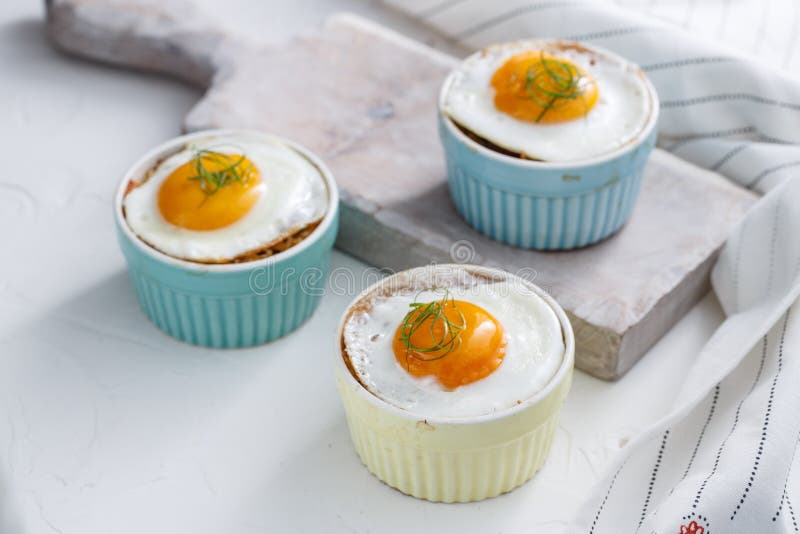 Three baked egg in ramekins on white background. Three baked egg in ramekins on white background.